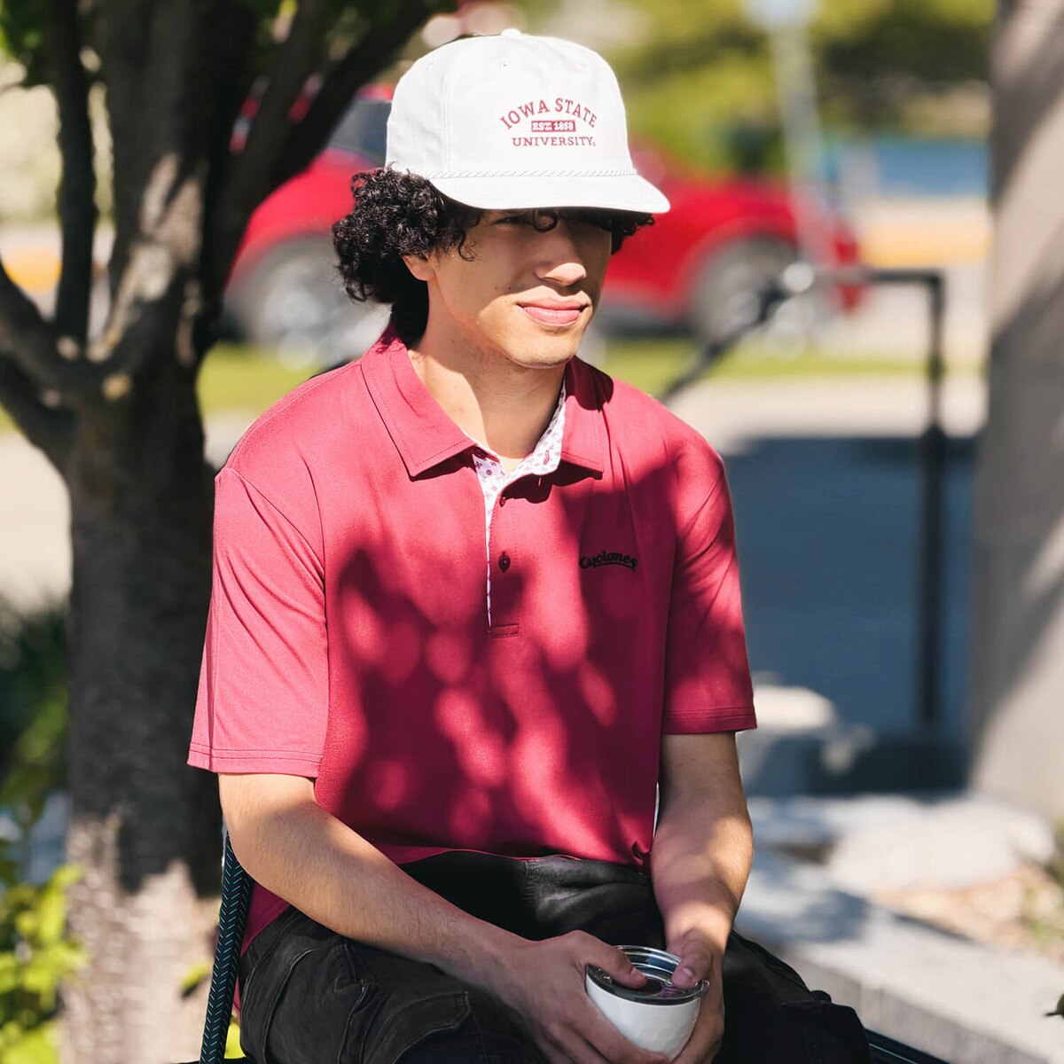 Student sitting on the bench wearing Swannies Cyclones Script Cardinal James H Polo and a matching Swannies hat